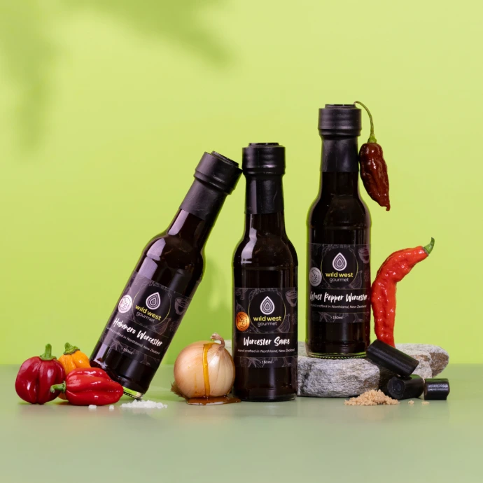 Three bottles of worcester sauce, one jauntily leaning, on another bottle, with a crisp green backdrop